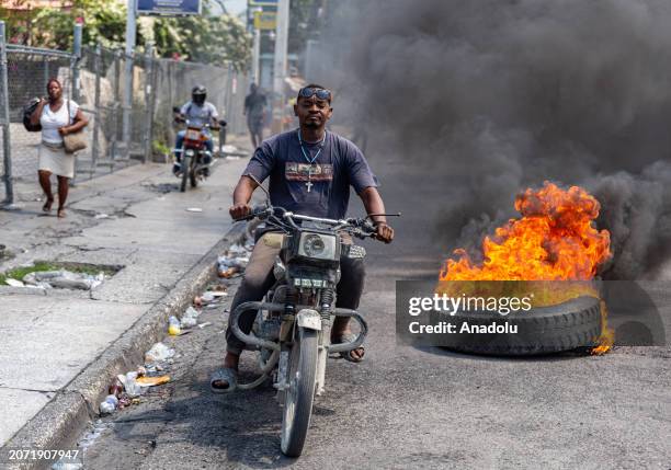 Motorcyclist passes burning tires during a demonstration against CARICOM for the decision following the resignation of Haitian Prime Minister Ariel...