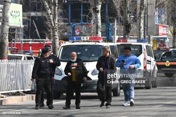 People walk past police vehicles opposite to the site of a suspected gas explosion in Sanhe, in China's northern Hebei province on March 13, 2024. A...
