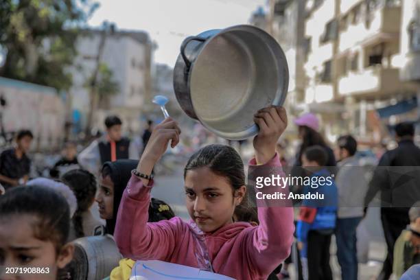 Palestinian children holding banners and empty bowls, gather to protest the food shortages in the city due to Israeli attacks and demanding a...