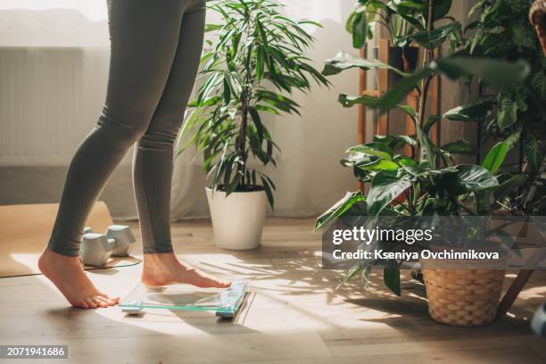 a young woman is weighing herself in a weighing scale - weegschaal stockfoto's en -beelden