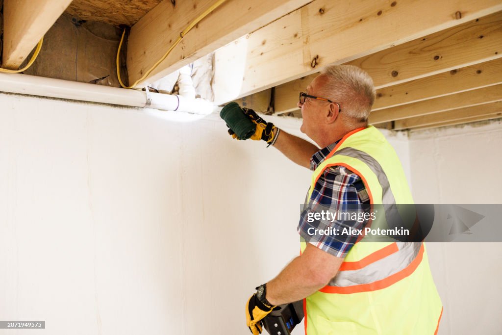 Checking pipes and insulation after water damage. Mature claim agent in vest highlight water pipes, quality control indoors