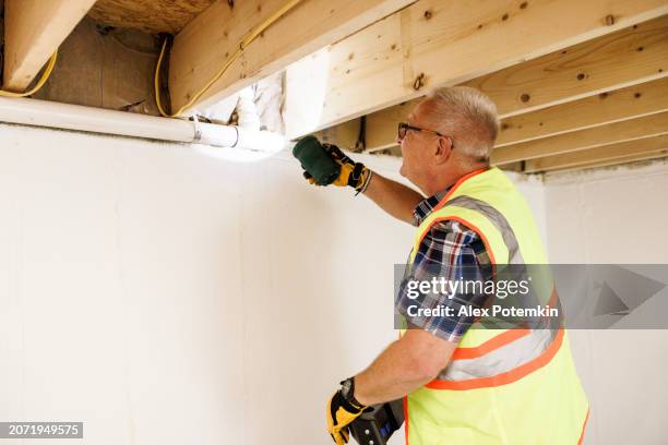 checking pipes and insulation after water damage. mature claim agent in vest highlight water pipes, quality control indoors - controlo de qualidade imagens e fotografias de stock