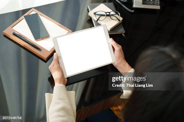 over the shoulder view an asian woman's hand is seen using a digital tablet while working from home, illustrating the blend of lifestyle and technology. - ipad mockup stock pictures, royalty-free photos & images