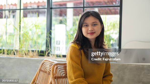 portrait of happy young asian girl wearing yellow clothes at cafe looking at camera - indonesische etniciteit stockfoto's en -beelden