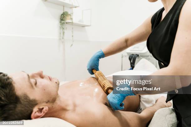 man receiving a massage with wooden roller in modern spa center - estilo de vida alternativo fotografías e imágenes de stock