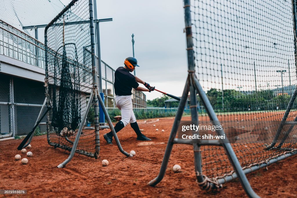 A baseball batter is practicing hitting skills inside a portable protective net.