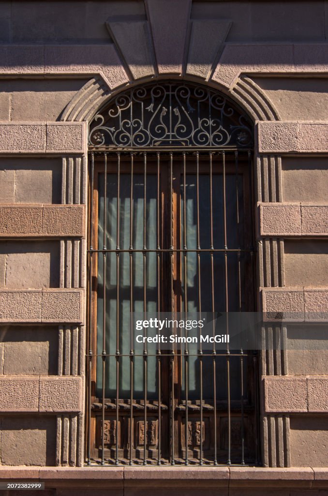 Elegant Neo-classical carved pink quarry stone colonial mansion building facade with an arched window and decorative wrought iron grille
