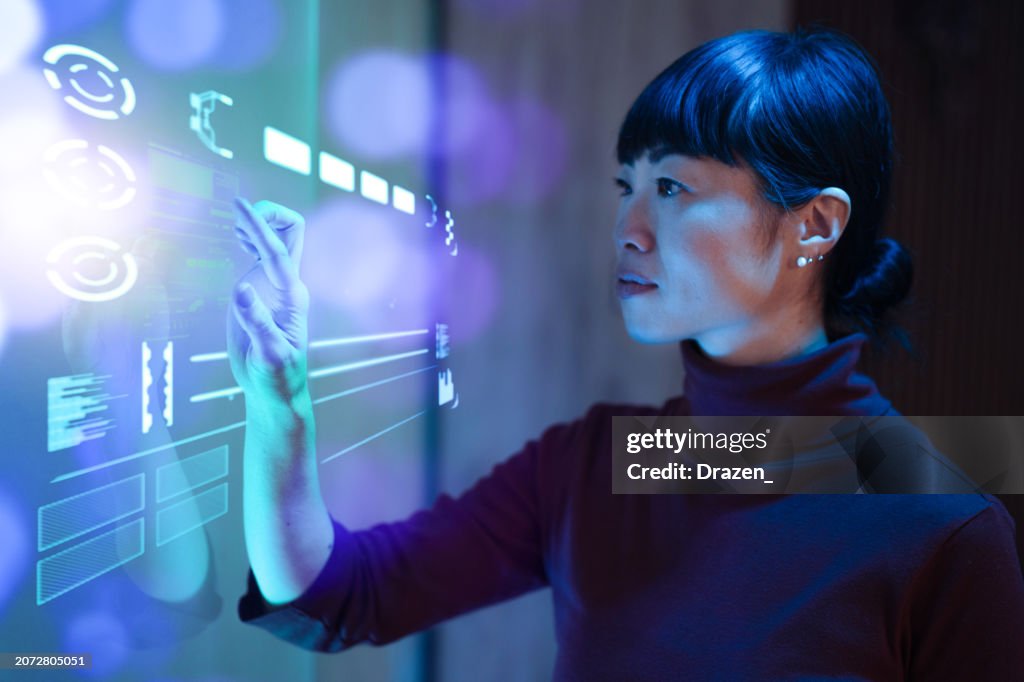 Futuristic office with Japanese mature businesswoman working on touchscreen and making decisions