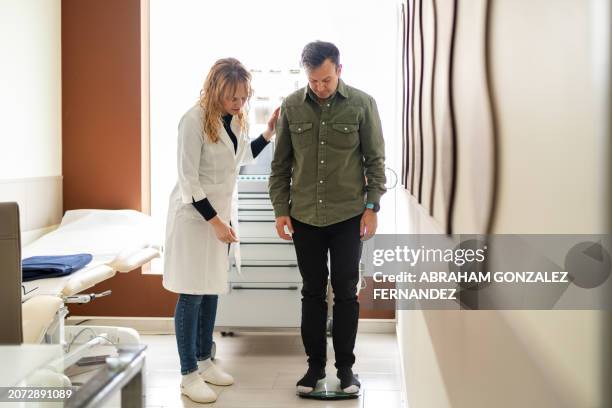 doctor measuring a man's weight with a scale at the clinic - nutritionist stock pictures, royalty-free photos & images
