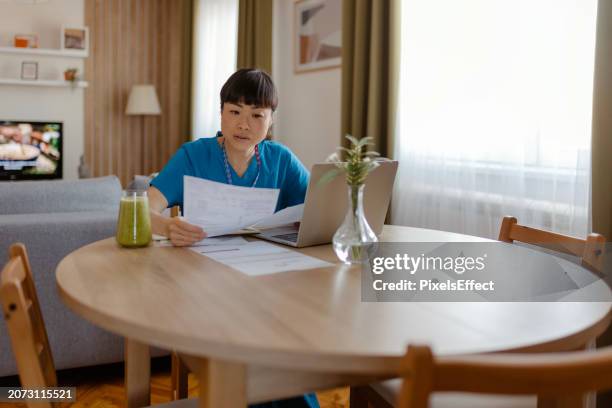 asian female healthcare worker doing paperwork at home - entrepreneur stockfoto's en -beelden