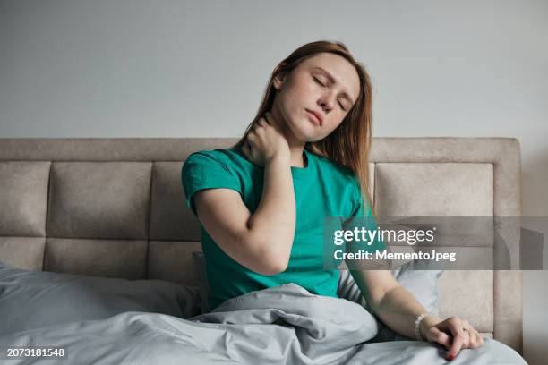 tired exhausted woman sits in bed touching neck, suffering from neck pain, sleeping on uncomfortable pillow - neck stretch stock pictures, royalty-free photos & images