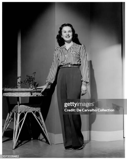 Publicity portrait of Canadian actor and singer Deanna Durbin standing up beside a table United States.