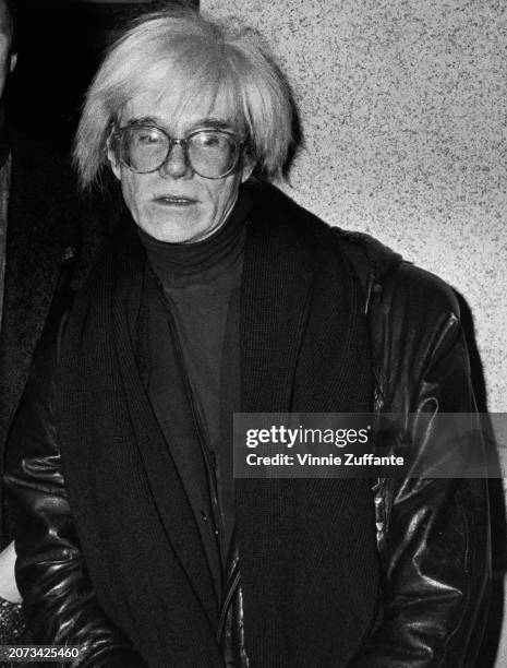 American artist Andy Warhol wearing a leather jacket over a turtleneck sweater with a scarf, attends a party at The Gotham, a restaurant in...