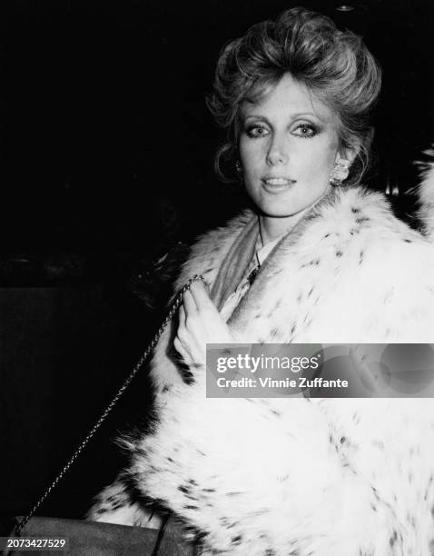 American actress Morgan Fairchild, wearing a fur coat and holding her purse by its chain shoulder strap, attends the Night of 100 Stars II Gala, held...