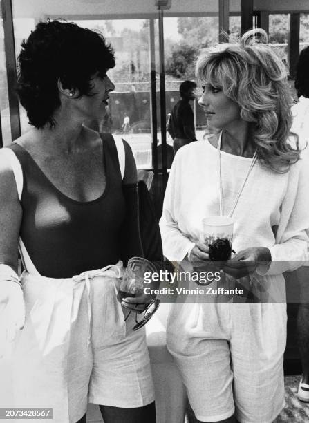 Canadian-American actress Beverly Sassoon and American actress Morgan Fairchild, both holding disposable cups and sunglasses, United States, circa...