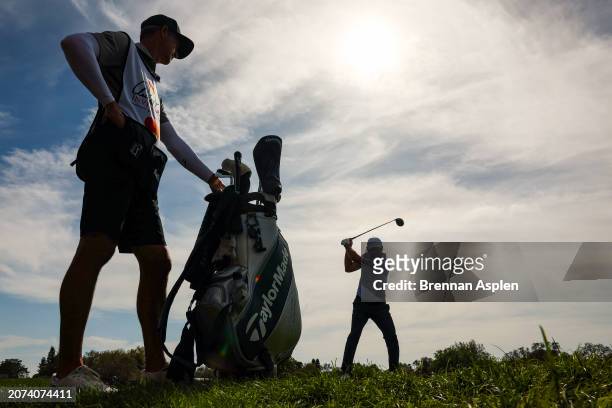 Scottie Scheffler of the United States hits a tee shot on the 12th hole as his caddie Ted Scott looks on during the final round of the Arnold Palmer...