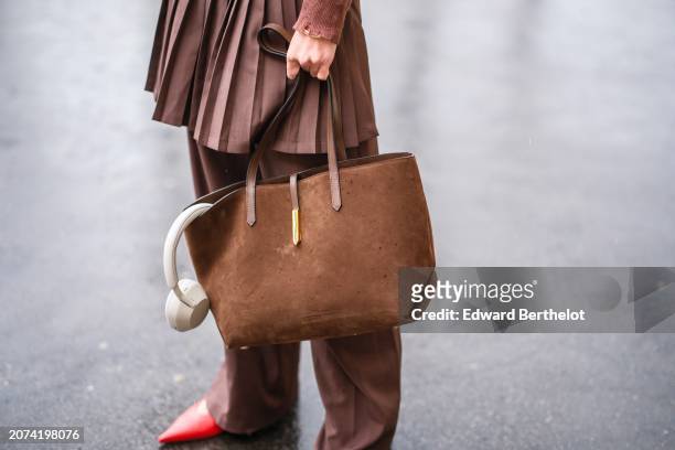 Natalia Verza wears brown flared pants, a mini brown pleated skirt by Frankie shop, a large brown suede bag from DeMellier containing headphones,...