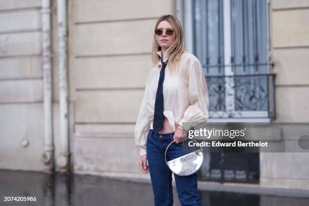 Natalia Verza wears Capri low waist dark blue denim cropped pants from Prada, a transparent gathered beige shirt from Munthe, a blue tie by Chanel, a...