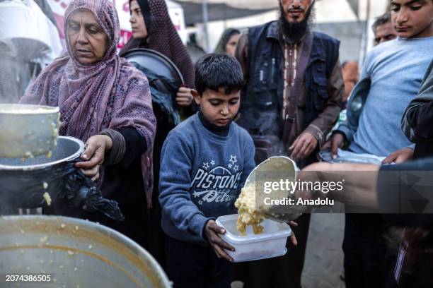 Palestinians line up to receive food, distributed by aid organizations, on the third day of Ramadan as Israeli attacks continue in Deir al-Balah,...