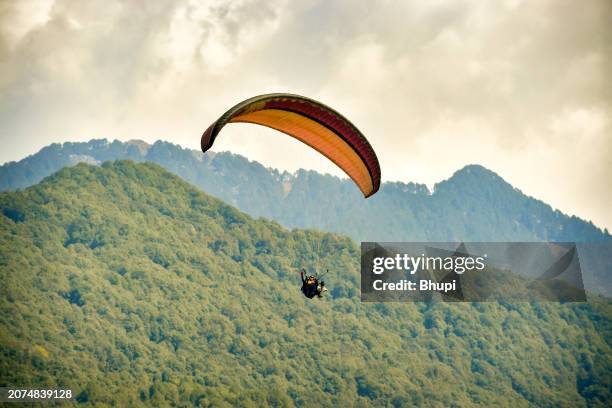 young man flying on a paraglider with an instructor in the mountains - glider stock pictures, royalty-free photos & images