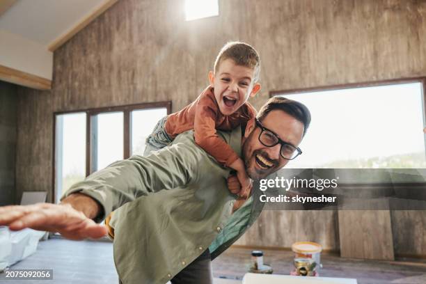 playful father and son having fun while piggybacking in new home. - milestone stockfoto's en -beelden