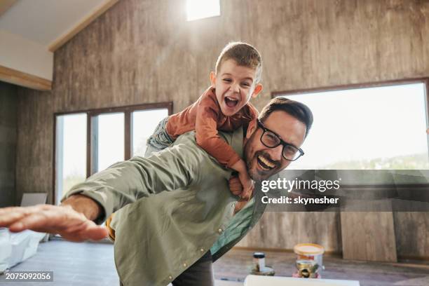 playful father and son having fun while piggybacking in new home. - piggyback stock pictures, royalty-free photos & images
