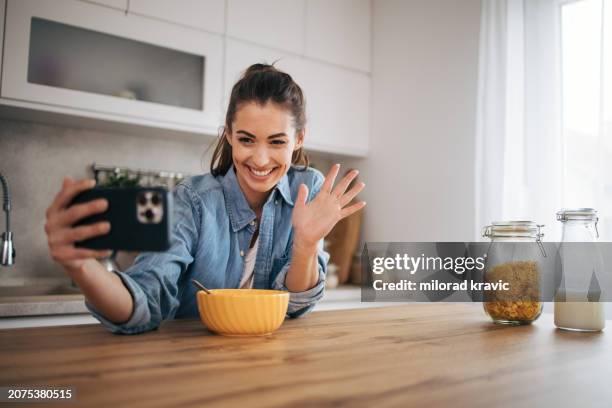 young woman using the mobile phone while eating cereal with milk - milk stream stock pictures, royalty-free photos & images