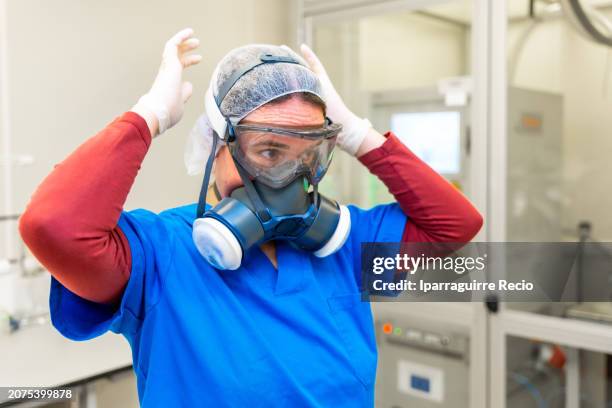 scientist putting on protective gear to enter a machine for electrical tests with plasma - atemschutzmasken stock-fotos und bilder
