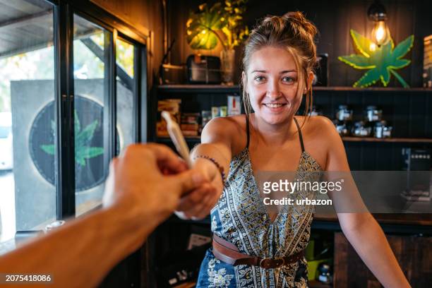 young woman giving a marijuana joint to a customer in a cannabis shop in thailand - a j price stock pictures, royalty-free photos & images
