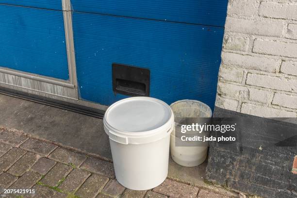 white plastic buckets stand outside in the corner of a garage door - yoghurt lid stock pictures, royalty-free photos & images