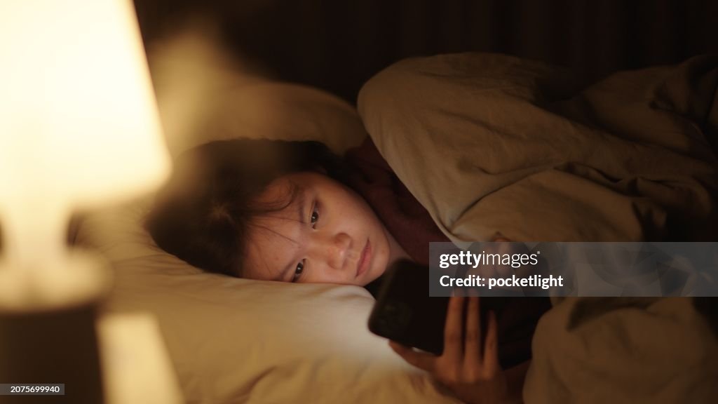 Girl using smartphone on bed at night.