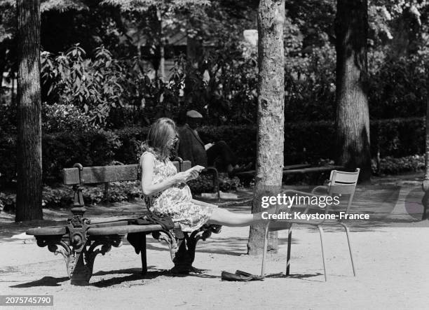 Parisienne profitant du soleil sur un banc dans le jardin des Tuileries à Paris, le 11 mai 1964.