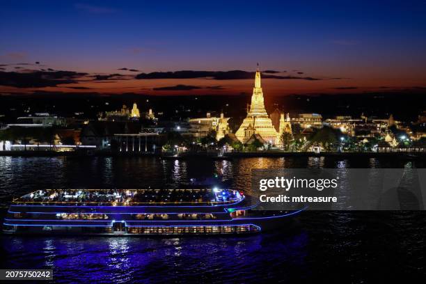 close-up image of dinner cruise boat passing wat arun (temple of dawn) viewed across chao phraya river, illuminated waterfront view, bangkok, thailand, reflections in water at twilight, focus on foreground - chao phraya river stock pictures, royalty-free photos & images