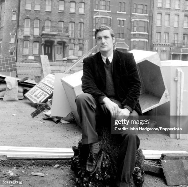 English poet and writer Ted Hughes seated on a tree stump on a residential street in London in 1959.