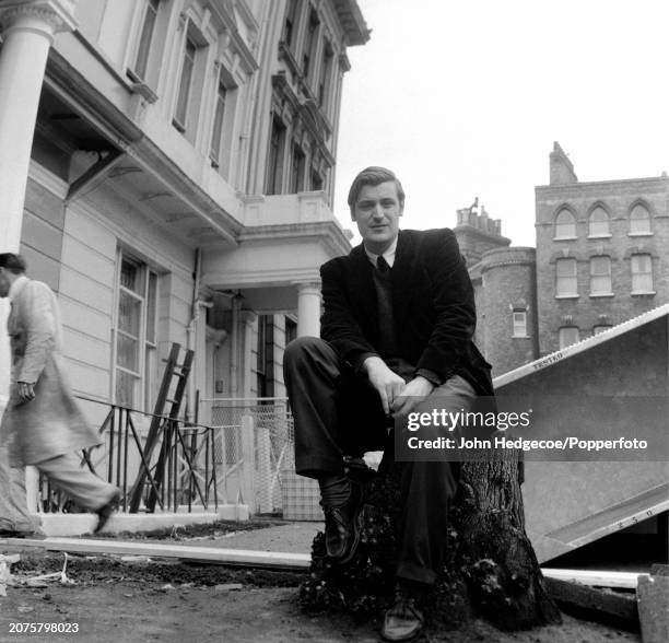 English poet and writer Ted Hughes seated on a tree stump on a residential street in London in 1959.