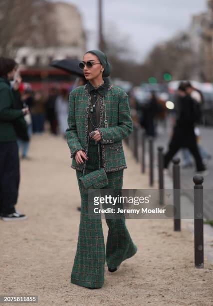 Guest wears green hijab or a head scarf, green checkered blazer, matching checkered green pants, shoes, Chanel necklaces outside Chanel show, during...