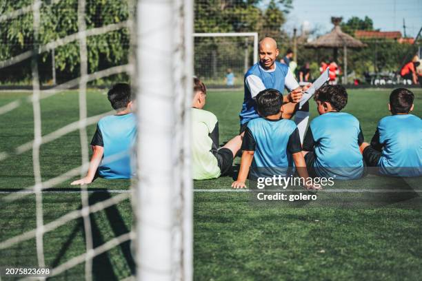 coach sitting with boy soccer team on pitch and drawing on match board - soccer competition stock pictures, royalty-free photos & images