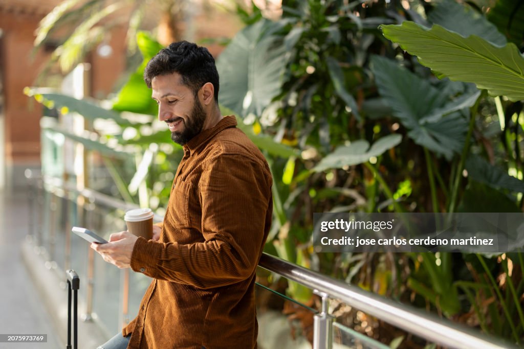 Smiling Man with Mobile Phone and Coffee Outdoors