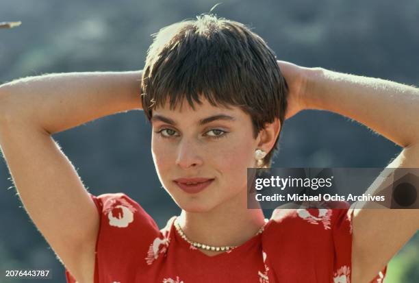 German actress and model Nastassja Kinski, wearing a red top, with heart-shaped earrings, her hands behind her head, United States, December 1980.