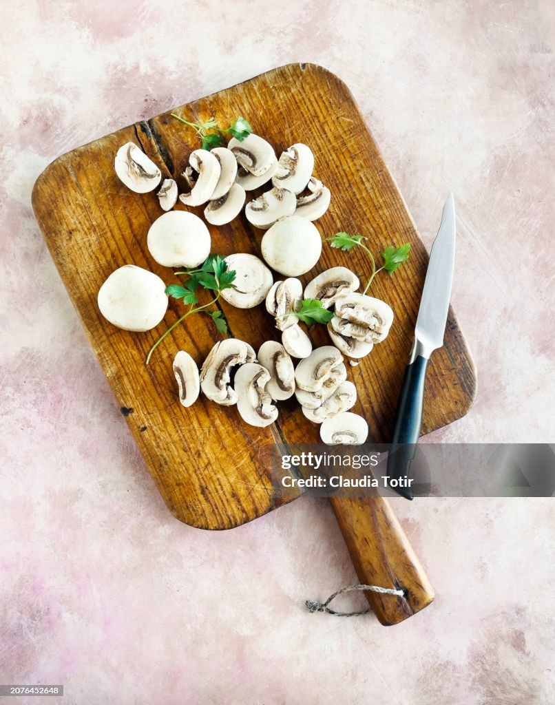White button mushrooms on wooden cutting board on pink weathered background