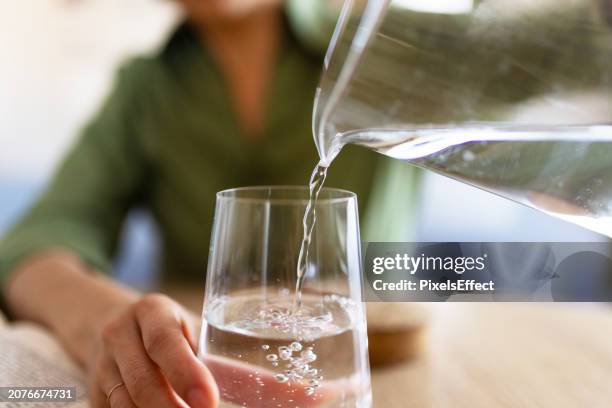 mujer vertiendo agua de jarra en vidrio - agua potable fotografías e imágenes de stock