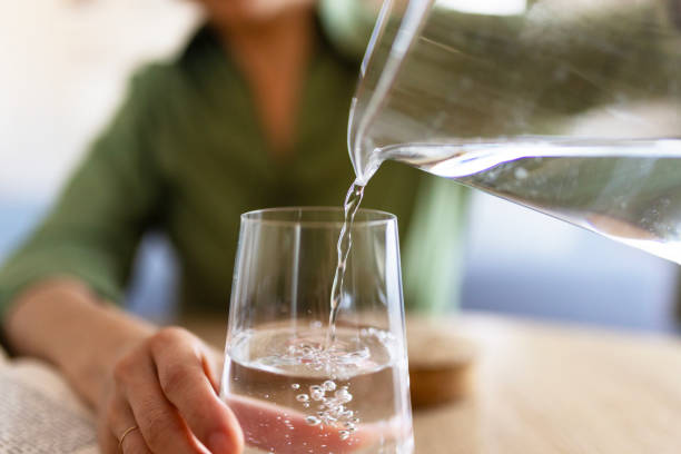 woman pouring water from jug into glass - hydration stock pictures, royalty-free photos & images