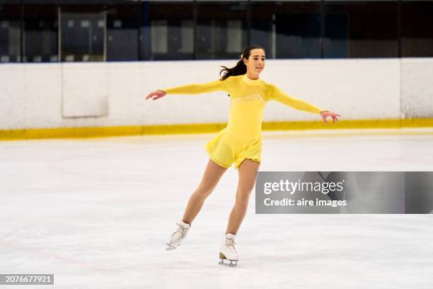 portrait of a young woman smiling wearing a full yellow dress while practicing figure skating on an ice rink, front view - ice skater stock pictures, royalty-free photos & images