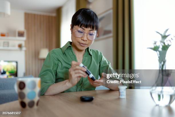 asian woman using a glucose monitoring device at home - glucose stockfoto's en -beelden