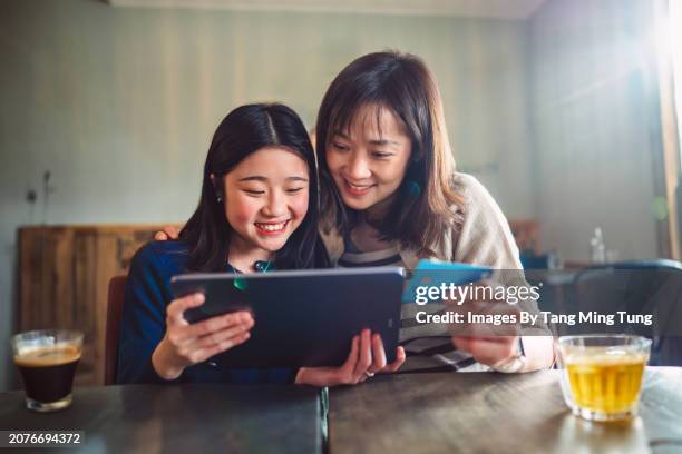 cheerful asian mom & daughter shopping online with credit card on digital tablet while enjoying coffee break in cafe. building good financial habit for teens concept. - retail equipment stock pictures, royalty-free photos & images