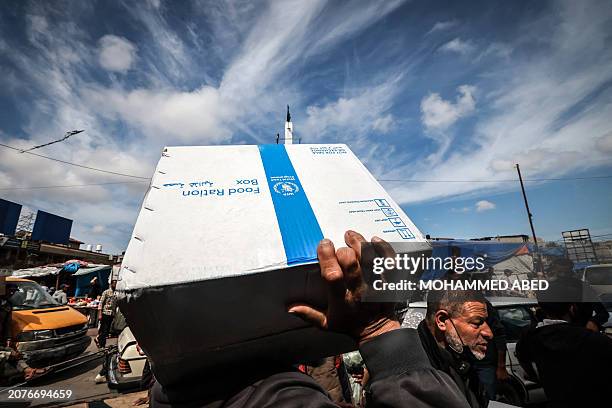 Displaced Palestinians carry a box of food rations provided by the World Food Programme at a makeshift street market in Rafah in the southern Gaza...
