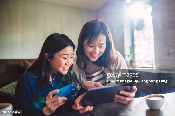 cheerful asian mom & daughter shopping online with credit card on digital tablet while enjoying coffee break in cafe. building good financial habit for teens concept. - retail equipment stock pictures, royalty-free photos & images