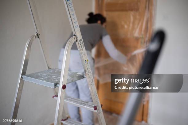 February 2024, Berlin: A woman tapes a door in a room before painting. Photo: Sebastian Gollnow/dpa