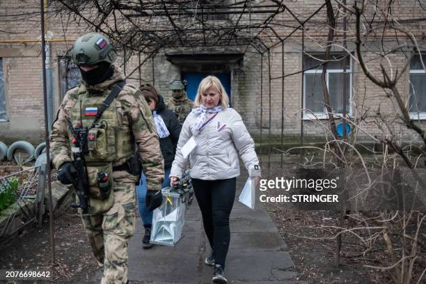 Members of a local election commission, accompanied by servicemen, visit voters during early voting in Russia's presidential election in Donetsk,...
