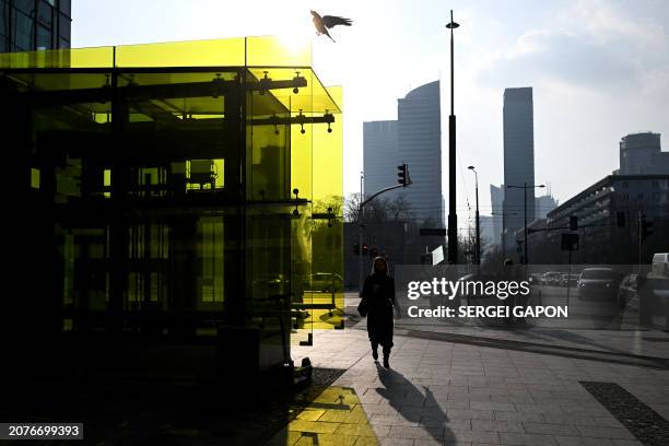 Bird lands on the glass as a woman walks down the street during a sunny day in Warsaw, Poland on March 14, 2024.